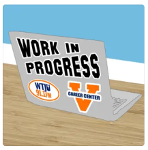 Open laptop on wooden desk with "Work in Progress" sticker